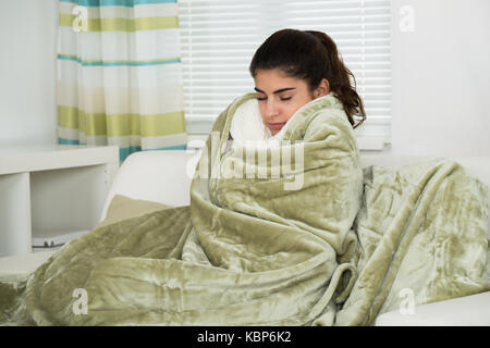 Giovane donna coperta con coperta soffrono di freddo a casa Foto Stock