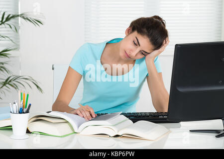 Stanco studentessa con la mano sulla testa che studiano in home office Foto Stock