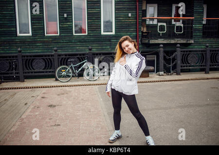 Giovane donna che mostra pollice in alto segno prima di correre sulla bicicletta . outdoor sport concetto. verde sullo sfondo della parete Foto Stock