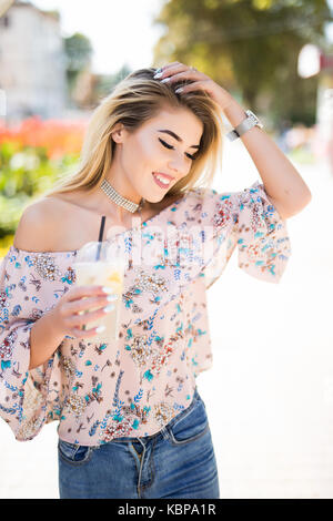 Godetevi ogni momento. close-up di bella e giovane ragazza sorridente di bere la limonata e tenere il telefono in mano mentre passeggiando per le strade delle città. Foto Stock