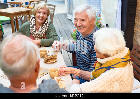 Gioiosa amici anziani avente tea party al meraviglioso outdoor cafe: essi godendo di pasticceria e caffè fragrante e chiacchierando animatedly gli uni con gli altri Foto Stock