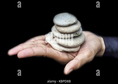 Una mano che tiene ciottoli accatastati gli uni sugli altri. Foto Stock