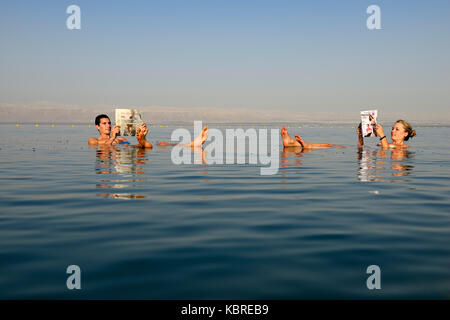 Coppia giovane legge giornale galleggianti nel mar morto, Giordania Foto Stock