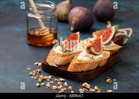 Panini con fichi, ricotta, miele, noci, fichi freschi e un vaso di miele su uno sfondo blu Foto Stock