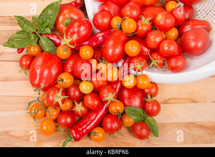 Pomodori freschi, peperoni, con basilico riversandosi su di un tagliere Foto Stock