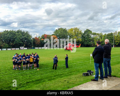 Woodford Green, Londra, Regno Unito. Il 30 settembre 2017. Funzionari guardare come London Air Ambulance elicotteri G-LNDN atterra a Woodford Rugby Football Club Highams massa nel Woodford Green in risposta a una relazione di uno spettatore la sofferenza di un attacco di cuore. Il Woodford v Chelmsford match è stato sospeso per 40 minuti mentre i paramedici hanno partecipato alla vittima che era in grado di uscire dalla strada. Woodford è andato a vincere la partita. La Air Ambulance è supportato da Londra massoni. Credito: Mark Dunn/ Alamy Live News Foto Stock