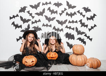 Paio di due divertenti bambina vestito in costumi di halloween in posa mentre è seduto con zucche e pipistrelli su uno sfondo Foto Stock