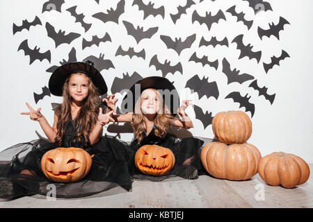 Paio di due bambina vestito in costumi di halloween in posa mentre è seduto con zucche e pipistrelli su uno sfondo Foto Stock