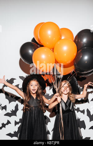 Paio di due bambine vestite in costumi di halloween trattenere aria palloni e posa con i pipistrelli su uno sfondo Foto Stock