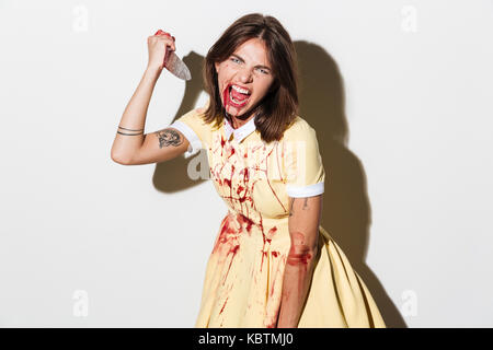 Donna di zombie con ferite e macchie di sangue in possesso di un coltello di grandi dimensioni e pronto ad attaccare isolate su sfondo bianco Foto Stock