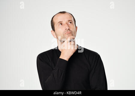 Uomo caucasico in camicia nera guardando in giù con emozione scettico sul viso. Foto Stock