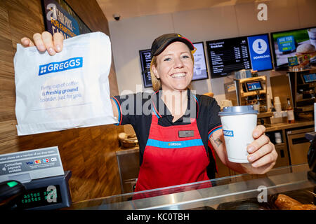 Shop lavoratore in servizio presso le casse di un Greggs in Bolton Interchange Foto Stock