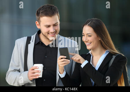 Vista frontale di due dirigenti felici parlando di smart phone contenuto all'esterno permanente sulla strada Foto Stock