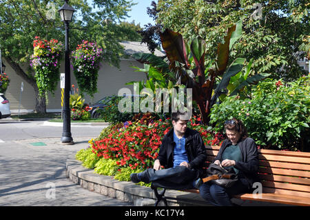 Due persone sedute su una panchina in un parco della città con giardini in background Foto Stock