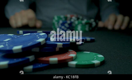 Close-up di uomo gettando un poker chips in slow motion. close-up di mano con gettando fiches su sfondo nero. poker player aumentando il suo stakes gettando i gettoni sul tavolo da gioco. Foto Stock