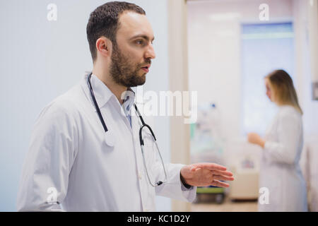 Pensieroso giovane medico in camice bianco tenendo la diagnosi in ospedale, caring concetto medico Foto Stock