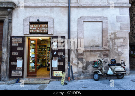 Spello, Perugia, Umbria, cuore verde d'Italia. un vecchio negozio di alimentari con prodotti tipici locali, come spello il pregiato olio d'oliva e avespa parcheggiata Foto Stock