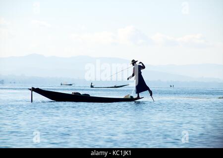 Lago Inle, myanmar - 15 novembre 2014. silhouette del pescatore intha canottaggio canoa con la sua gamba e tenendo la pesca net. Foto Stock