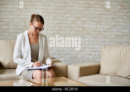 Ritratto di bellissima femmina psicologo indossando occhiali sulla scrittura di appunti in terapia office Foto Stock