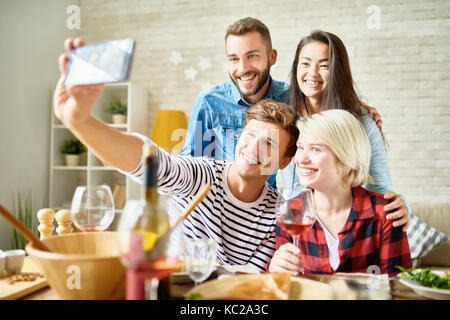 Ritratto di quattro amici felice tenendo selfie al tavolo per la cena mentre celebrava l occasione di festa insieme Foto Stock