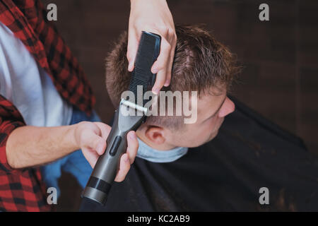 Giovani caucasici uomo in Barberia. Il Barbiere è cuttinhg i suoi capelli in hipster stile. Foto Stock