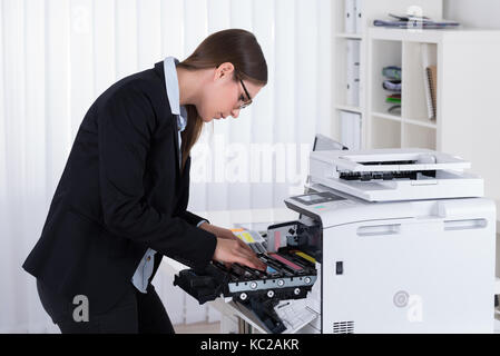 Giovane imprenditrice che fissa una macchina di copia al lavoro Foto Stock