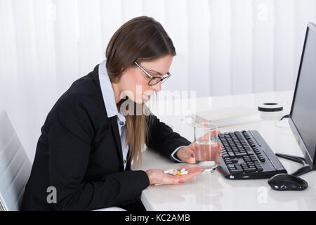 Contemplando l imprenditrice con le pillole e bicchiere di acqua alla scrivania in ufficio Foto Stock