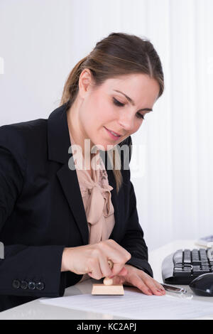 Giovane imprenditrice premendo francobollo di legno su carta alla scrivania Foto Stock
