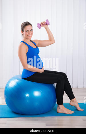 Felice incinta Donna seduta su sfera fitness facendo allenamento Foto Stock