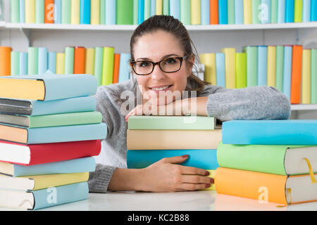 Donna felice appoggiato sulla pila di libri multicolore a scrivania Foto Stock