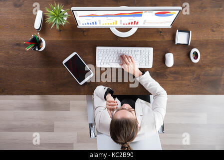Giovane imprenditrice Guardando grafici sul computer in ufficio Foto Stock