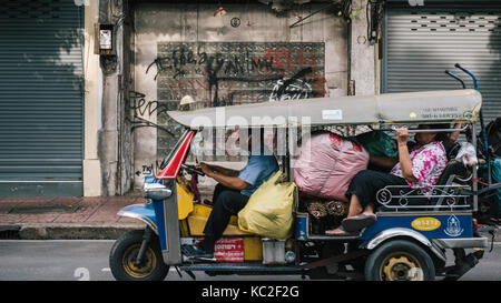 Un tuk tuk i trasporti di passeggeri e dei loro bagagli attraverso le strade di Chinatown a Bangkok, in Thailandia. Foto Stock