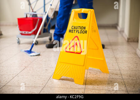 Sezione bassa del lavoratore pavimento con straccio con pavimento bagnato segno di attenzione sul pavimento Foto Stock