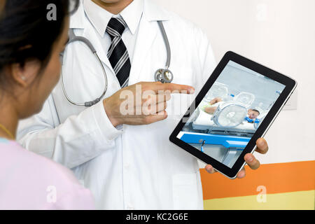 Smart healthcare tecnologia ospedaliera, intelligenza artificiale concetto. Medico utilizzano tablet schermo telemonitoraggio per mostrare neonato alla madre. Foto Stock