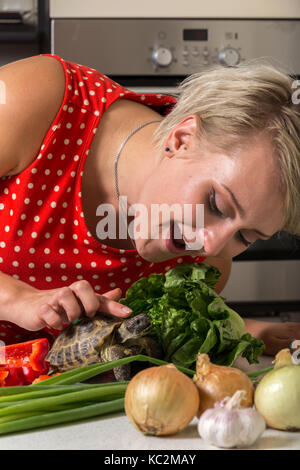 Ragazza inclinati verso il basso e il petting tartaruga sulla sua testa accanto al grande insalata romana Foto Stock