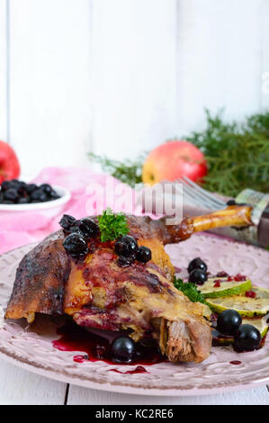 Oca al forno della gamba in salsa di frutti di bosco su una piastra di ceramica su un bianco sullo sfondo di legno. Foto Stock