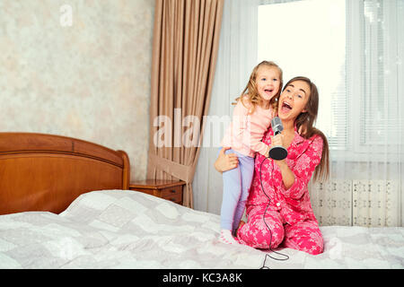 Madre e figlia cantare insieme divertimento brani karaoke in camera. Foto Stock