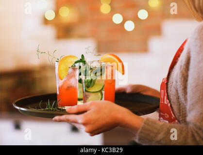 Giovane donna graziosa con il rosso e il verde cocktail sul vassoio in bar Foto Stock