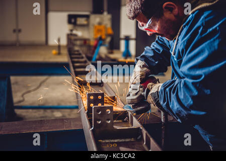 Lavoratore utilizzando smerigliatrice angolare in fabbrica e gettando scintille Foto Stock