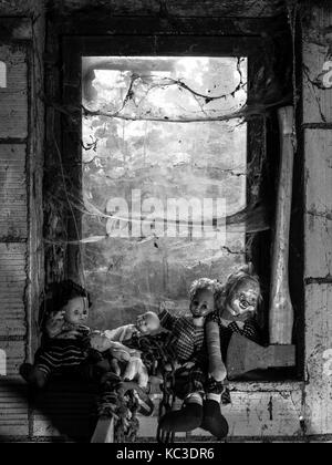 Foto del vecchio bambole e un'ascia in appoggio su un vecchio davanzale coperto di spiderwebs e polvere. Foto Stock