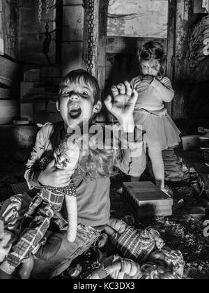 Foto di creepy giovani bambini in piedi sopra il vecchio bambole e in una stalla coperta in spiderwebs e polvere. Foto Stock