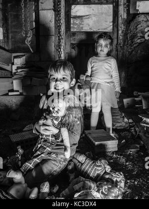 Foto di creepy giovani bambini in piedi sopra il vecchio bambole e in una stalla coperta in spiderwebs e polvere. Foto Stock