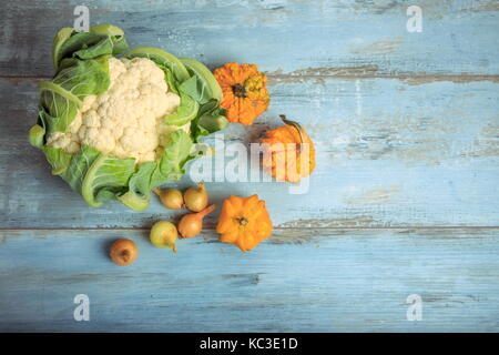 La zucca decorativa, cavolfiori e cipolle su un rustico in legno di colore blu sullo sfondo. il mangiare sano, concetto vegetariano. Foto Stock