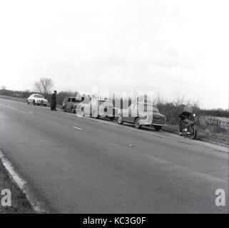 1964, storico, i funzionari di polizia in una Jaguar auto della polizia, un poilce Austin auto di Cambridge e una polizia Moto, indagare su un piccolo bruciato furgone parcheggiato in una piazzola di sosta accanto a una strada di campagna, Inghilterra, Regno Unito. Foto Stock