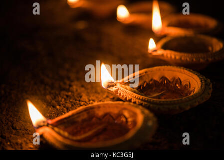 Felice diwali - molti diya in terracotta o lampade ad olio disposti sulla superficie di argilla o terra in una linea o curva o a zig-zag, il fuoco selettivo Foto Stock