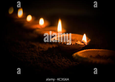 Felice diwali - molti diya in terracotta o lampade ad olio disposti sulla superficie di argilla o terra in una linea o curva o a zig-zag, il fuoco selettivo Foto Stock