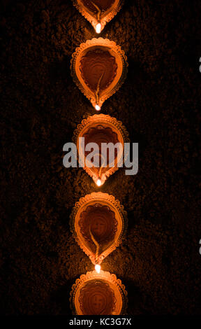 Felice diwali - molti diya in terracotta o lampade ad olio disposti sulla superficie di argilla o terra in una linea o curva o a zig-zag, il fuoco selettivo Foto Stock