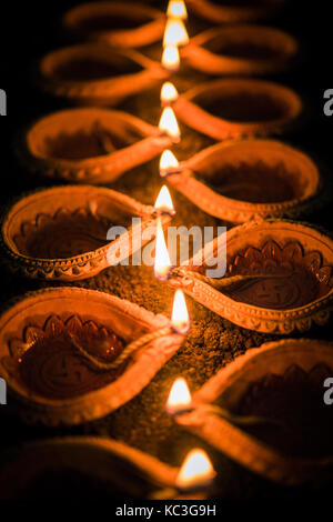 Felice diwali - molti diya in terracotta o lampade ad olio disposti sulla superficie di argilla o terra in una linea o curva o a zig-zag, il fuoco selettivo Foto Stock