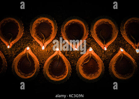 Felice diwali - molti diya in terracotta o lampade ad olio disposti sulla superficie di argilla o terra in una linea o curva o a zig-zag, il fuoco selettivo Foto Stock