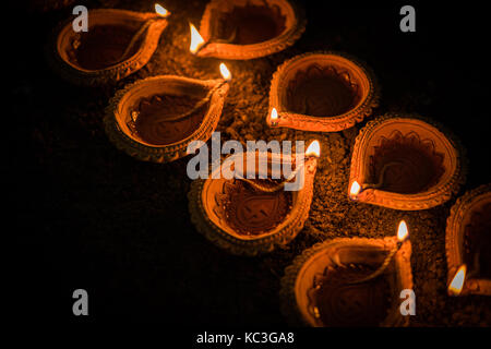 Felice diwali - molti diya in terracotta o lampade ad olio disposti sulla superficie di argilla o terra in una linea o curva o a zig-zag, il fuoco selettivo Foto Stock